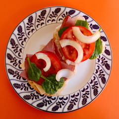 Pastrami on a bun with cheese, tomato and onion.