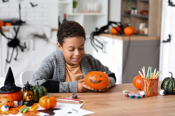 Teenage African-American boy with painted Halloween pumpkin at home