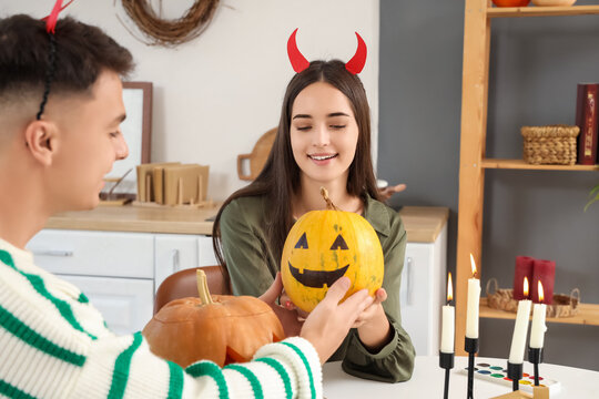 Young happy couple with Jack-O-Lantern pumpkins in kitchen decorated for Halloween party - Powered by Adobe