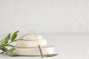 Acupuncture needles and spa stones on light background