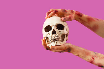 Zombie hands with human skull on pink background. Halloween celebration