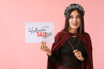 Beautiful young happy Asian woman dressed as witch with magic wand and text HALLOWEEN SALE on pink...