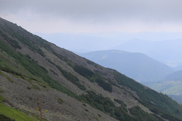 Fototapeta premium Tall Mountain Peaks with Green Slopes and Light Clouds
