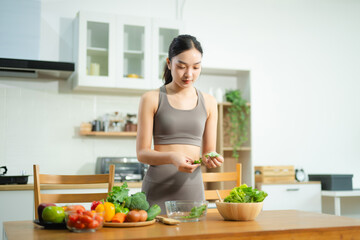 Asian woman prepares fresh vegetable salad in home kitchen. Healthy lifestyle, clean eating, wellness, and fitness food prep concept.
