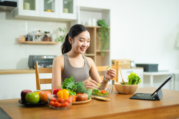 Asian woman holding green juice and apple, surrounded by fresh vegetables and salad in modern kitchen. Promotes healthy eating, fitness, and wellness lifestyle.