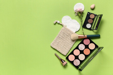 Composition with cotton pads, flower, makeup products and brush on green background