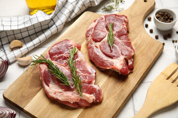 Wooden board with fresh raw steaks and different spices on white tile background, closeup
