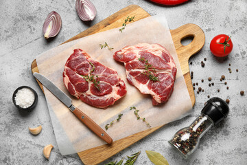 Wooden board with fresh raw steaks and different spices on grey background