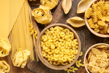 Bowls with different types of pasta on wooden background, closeup