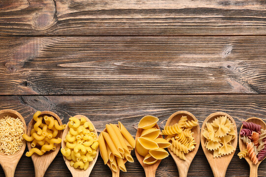 Wooden spoons with different types of pasta on wooden background