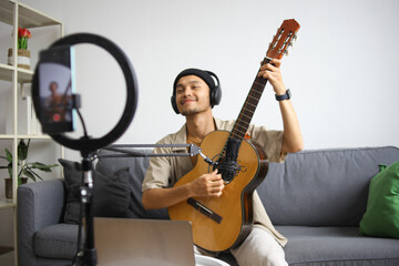 Smiling Musician With Headphones Raising Acoustic Guitar, Performing For Online Audience