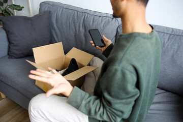 Frustrated Young Asian Man On The Phone Expressing Disbelief With Open Box Of Shoes