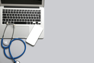 Mobile phone with modern laptop and stethoscope on grey background