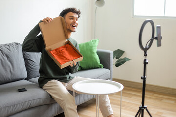 Friendly Male Influencer Reviewing Product On Cardboard Box During Live Streaming
