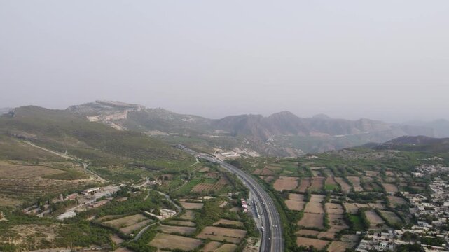 Wide aerial of M2 Motorway winding through green fields and hills in Kallar Kahar. Pakistan