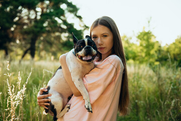 Teenage girl hugs her pet dog, a French bulldog, in nature, at sunset