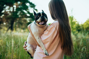 Teenage girl holds her pet's beloved dog in her arms, turning her back in the park, in the garden