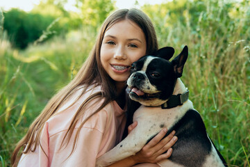 Portrait of a happy teenage girl and her beloved pet dog at sunset in the park, in the garden. The dog is a French bulldog of black and white color