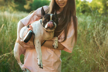 Teenage girl on a walk with her pet dog French bulldog. He holds her in his arms. Crop.
