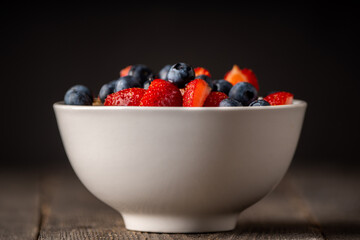 Oatmeal with ripe strawberries, blueberries and honey in the bowl. Selective focus.