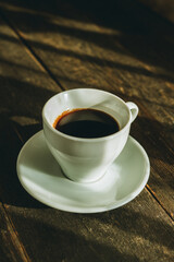 Cup of coffee on the wooden table. Warm colors of morning sunshine.
 Selective focus.