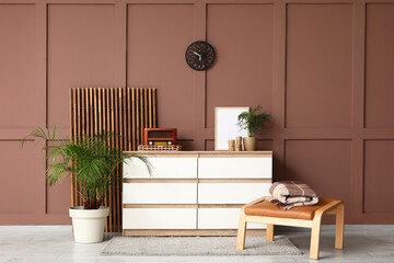 Chest of drawers, folding screen and foot stand near brown wall in interior of room