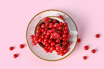 Cup with ripe red currant on pink background, closeup