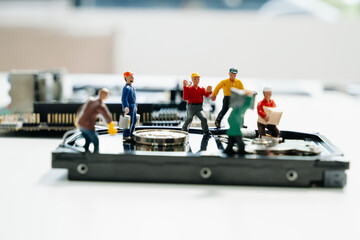 Creative tech concept showing miniature workers repairing an open hard disk drive on a motherboard. Symbolizes data recovery, repair, and computer maintenance.
