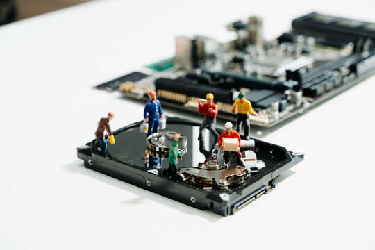 Creative tech concept showing miniature workers repairing an open hard disk drive on a motherboard. Symbolizes data recovery, repair, and computer maintenance.