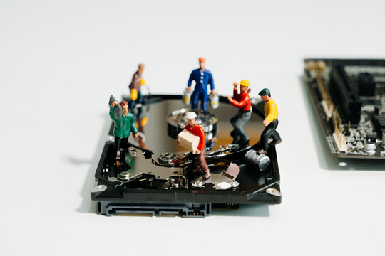 Creative tech concept showing miniature workers repairing an open hard disk drive on a motherboard. Symbolizes data recovery, repair, and computer maintenance.