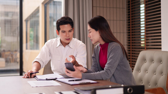 Asian business professionals discuss project strategy using smartphone in modern office setting collaborate on new ideas - Powered by Adobe