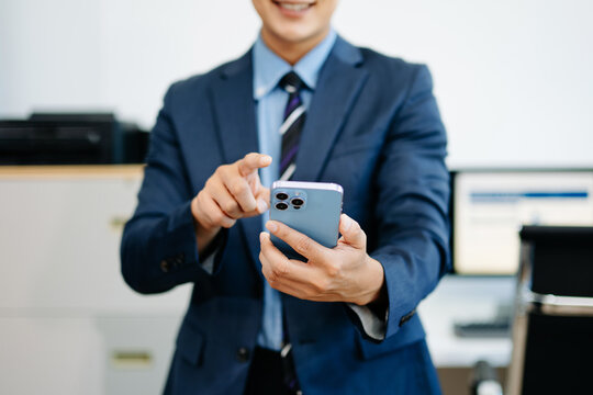 Smiling businessman in suit holds smartphone while gesturing to interact, symbolizing fintech, mobile ap