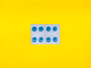 A blue pill is sitting on a white background. The pill is square in shape and has a blue center....