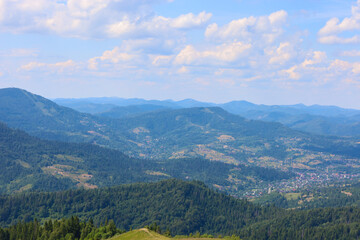 A mountain landscape with dense forests on the slopes that stretch to the horizon, where small villages are visible, creating a picturesque view.