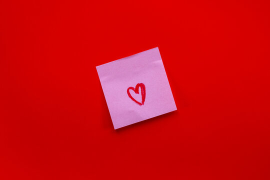 Pink sticky note with red heart drawing on vibrant red background for love notes or reminders