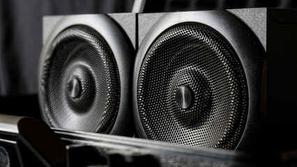 Close-up of black wooden hi-fi speakers with metal mesh grilles in a dark interior, capturing bass-rich audio technology for audiophile music playback. Photo
