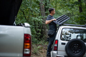 Driver securing recovery tracks to roof rack of off-road vehicle in forest © Zoran Jesic