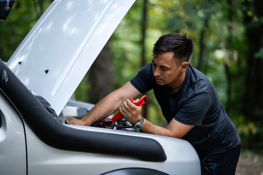 Driver connecting jumper cables to car battery in forest