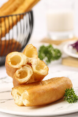 Delicious fried fritters displayed on a plate with a side of fresh herbs and accompanied by crispy snacks in a stylish basket