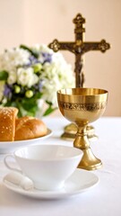 A brass chalice and crucifix sit on a table with bread and a white cup, set against a floral backdrop