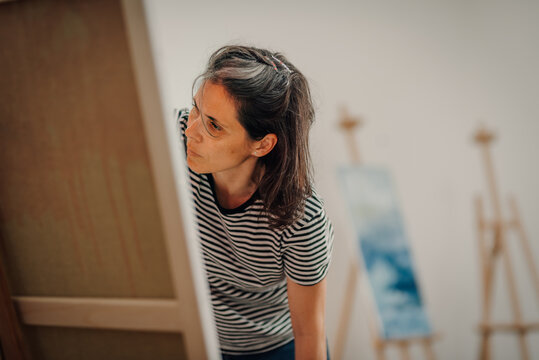 Female artist carefully examining her painting on canvas in art studio
