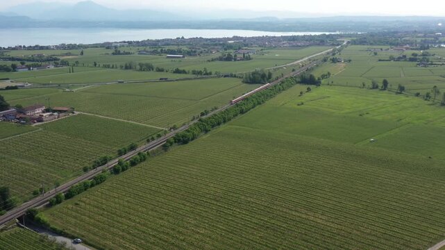 Aerial video of a red train racing through Italy&rsquo;s countryside, cutting through vineyards and rolling hills.