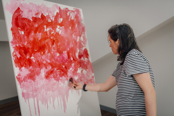 Female artist painting large abstract modern art painting using red and pink paint