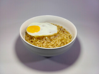 Round bowl containing a serving of instant noodles with a fried egg on top, topped with a few scattered, chopped onions and chili. Related to simple meals, comfort food, instant noodles, quick dishes
