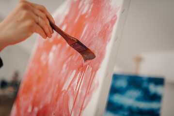 Artist painting red strokes on white canvas with brush in art studio
