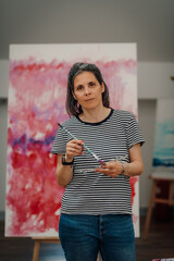 Female artist holding paintbrush and palette in art studio: painting colorful abstract artwork