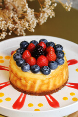 A delicious personal-sized cheesecake, topped with fresh strawberries, blueberries, and blackberries, is drizzled with red and yellow sauces on a white plate