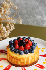 A delicious personal-sized cheesecake, topped with fresh strawberries, blueberries, and blackberries, is drizzled with red and yellow sauces on a white plate