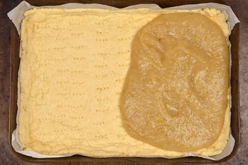 A rectangular baking pan with a partially baked pie crust, with cooked apple filling spread over approximately half of its surface
