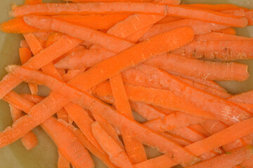 A close-up overhead shot reveals a textured pile of vibrant orange carrot peelings, indicating fresh vegetable preparation